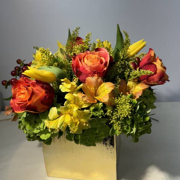 Orange and red roses with yellow flowers in a gold vase