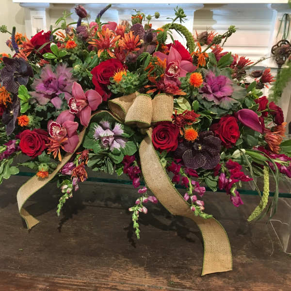 Large floral arrangement with red roses, orchids, and orange blooms tied with burlap ribbon