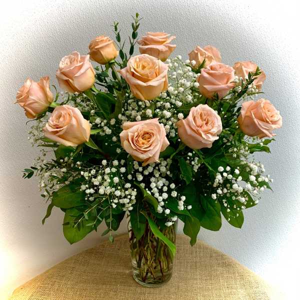 Peach roses arranged in a clear glass vase with baby's breath
