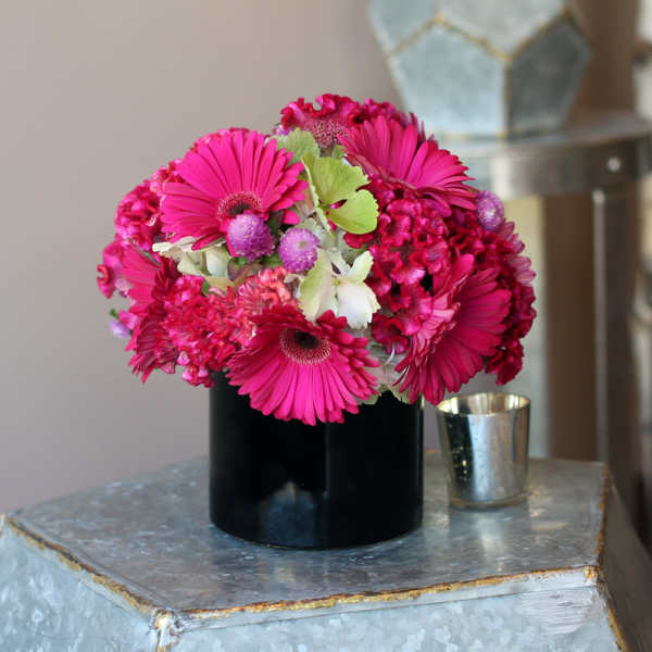 Bright pink gerbera daisies and mixed blooms in a black vase