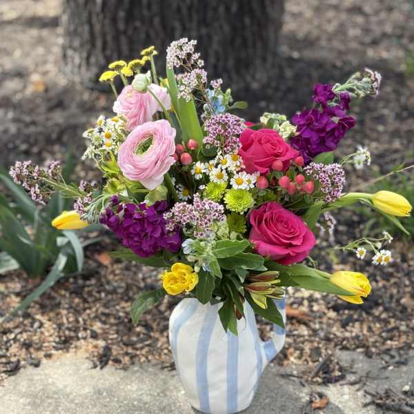 Colorful bouquet of pink roses, ranunculus, and yellow tulips in a striped ceramic pitcher.