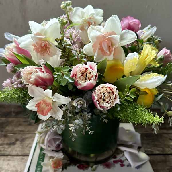 Mixed bouquet of white daffodils, pink tulips, and yellow blooms in a green vase