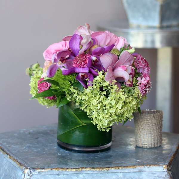 Pink and purple flowers arranged in a green glass vase