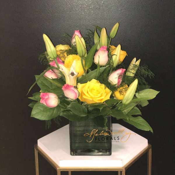 Yellow and pink roses with lily buds in a square glass vase