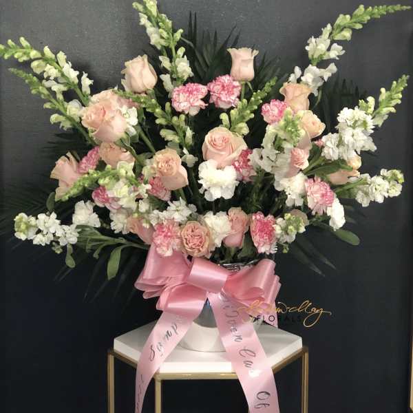 Large pink and white floral arrangement in a silver vase with a pink ribbon