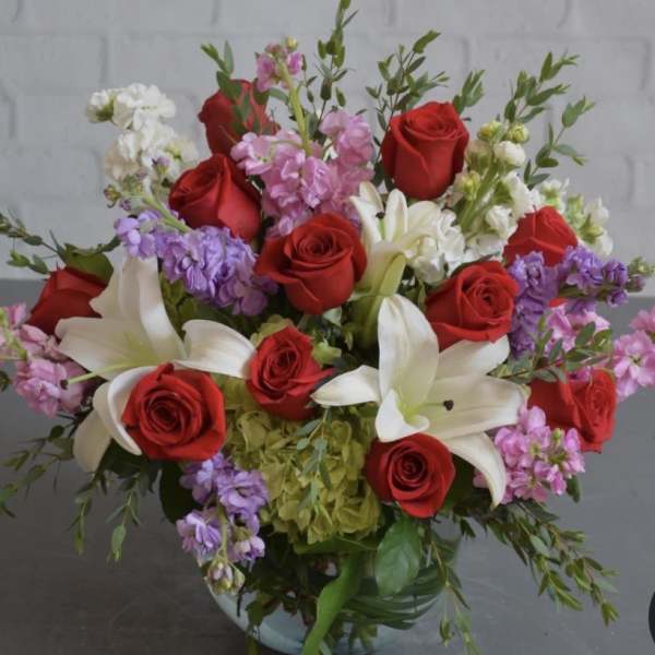 Bouquet of red roses, white lilies, and purple flowers in a vase