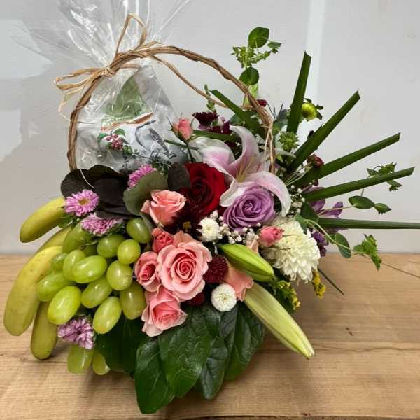 Fruit basket with roses, lilies, and grapes in a wicker handle wrap