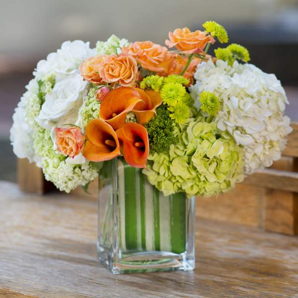 Bouquet of orange roses, white hydrangeas, and orange calla lilies in a glass vase