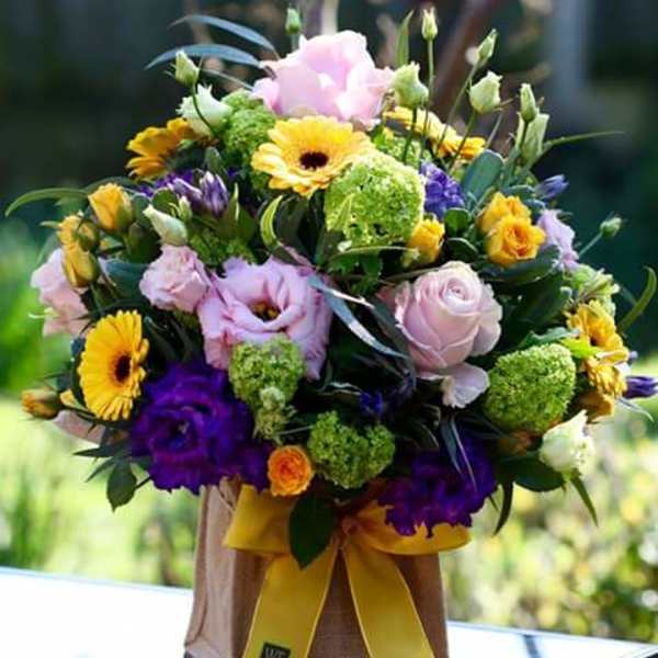 Mixed bouquet of pink, yellow, and purple flowers in a wrapped container