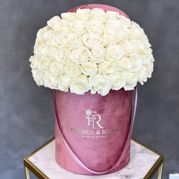 White roses arranged in a pink round box with ribbon handles