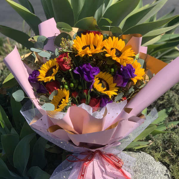 Bouquet of sunflowers and purple flowers wrapped in pink paper