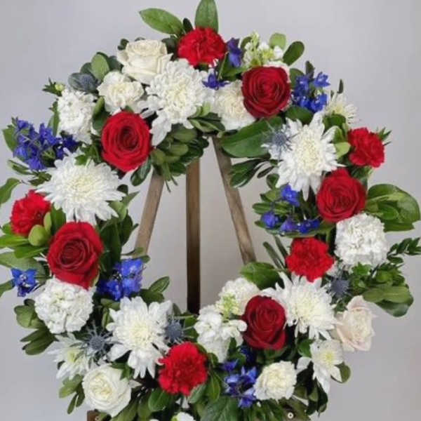 Circular floral wreath with red, white, and blue flowers on a wooden easel