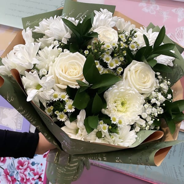 White bouquet of roses, chrysanthemums, and small daisies wrapped in green printed paper