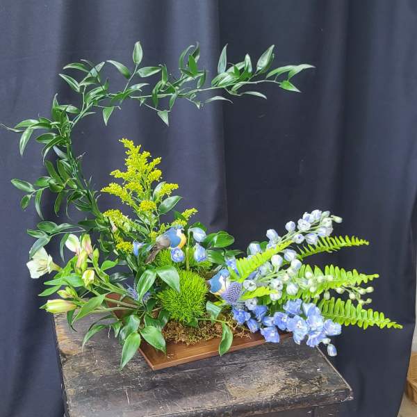 Floral arrangement with blue and white blooms in a wooden tray