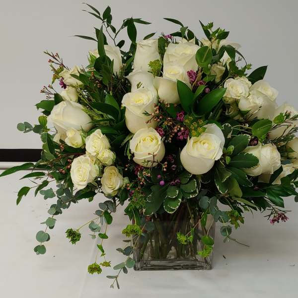 White rose bouquet in a clear glass vase with mixed greenery