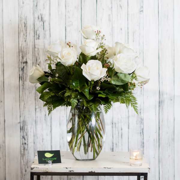 White roses arranged in a clear glass vase with greenery