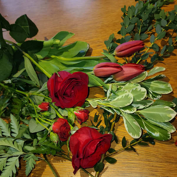 Red roses and pink tulips with assorted greenery on a wooden surface