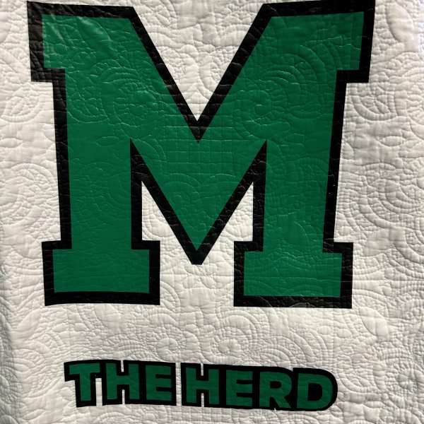 Quilt with a large green letter M and the words THE HERD