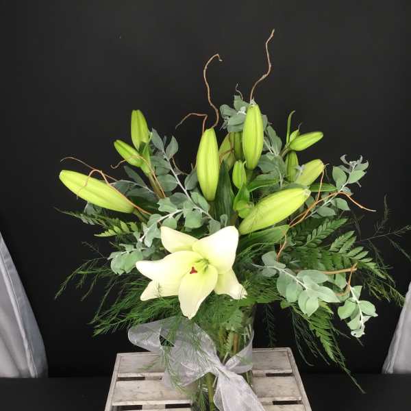 White lily arrangement in a glass vase with a sheer ribbon