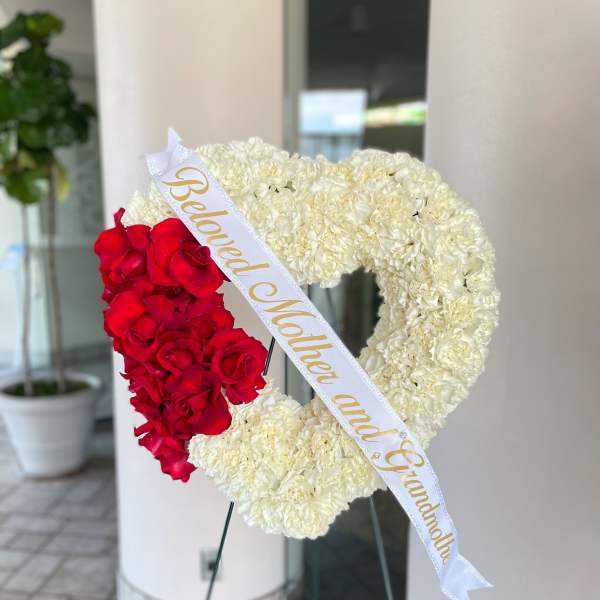 Heart-shaped floral wreath with red roses and white carnations on an easel