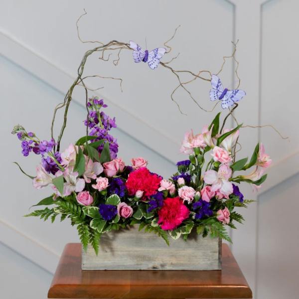 Pink and purple floral arrangement in a wooden box with butterfly picks