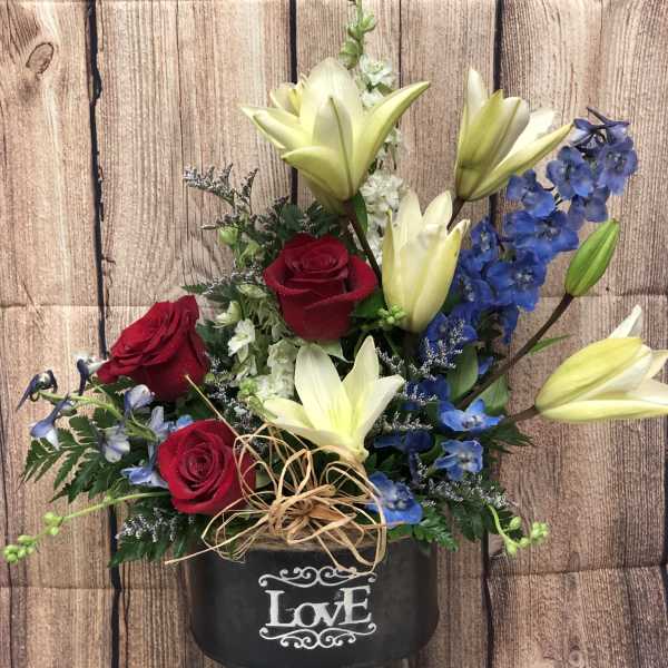 Red roses and pale lilies in a black container with a "Love" sign