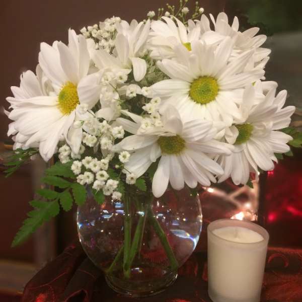 White daisy bouquet in a glass vase with a small candle beside it