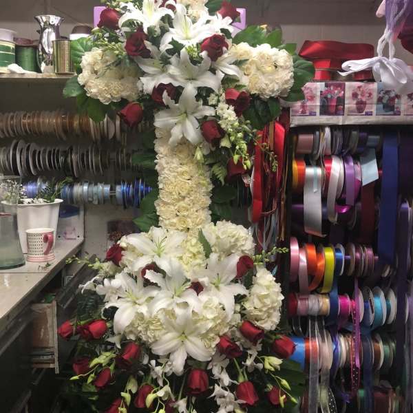 Tall floral cross with white lilies, cream roses, and red roses