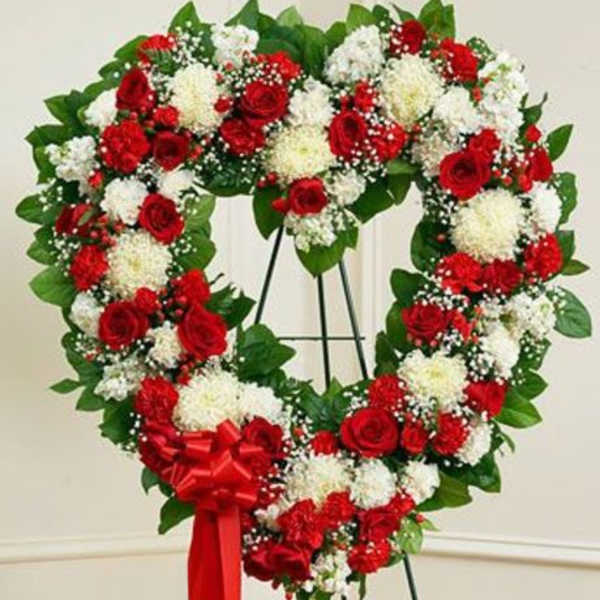 Heart-shaped wreath of red and white flowers on a stand with a red ribbon