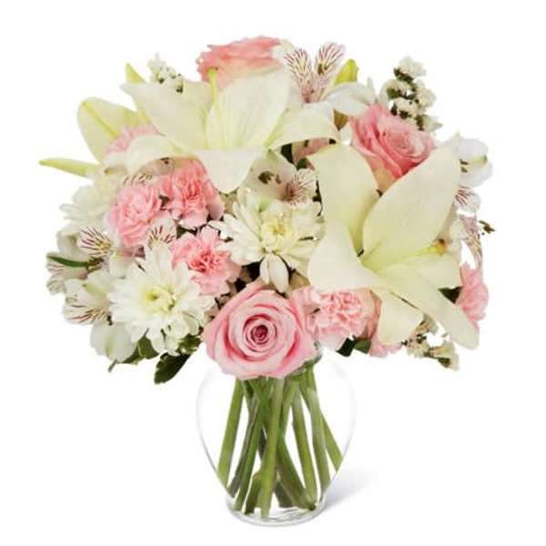 Pink and white bouquet of roses, lilies, and carnations in a clear glass vase