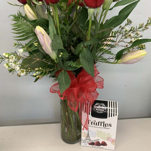 Red roses and lilies in a glass vase with a box of truffles