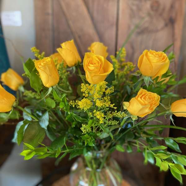 Tall arrangement of yellow roses in a clear glass vase with abundant greenery