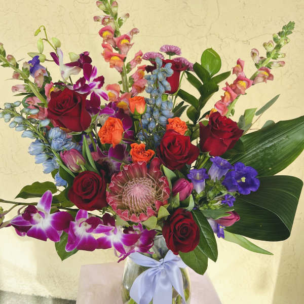 Mixed bouquet of red roses, orchids, and colorful blooms in a glass vase with ribbon
