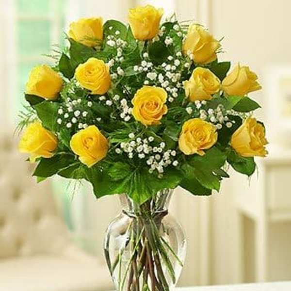 Yellow roses arranged in a clear glass vase with small white filler flowers.