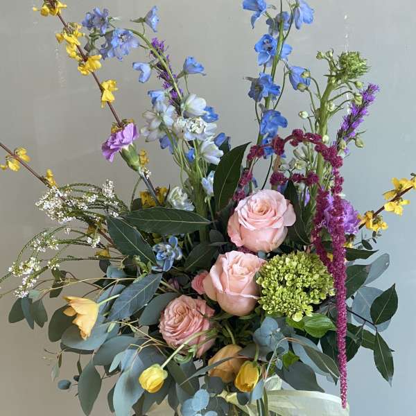Tall mixed bouquet in a glass vase with pink roses and blue flowers