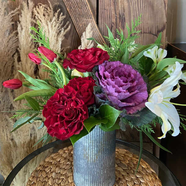 Tall corrugated metal vase with red roses, red tulips, purple ornamental cabbage, and white lilies.
