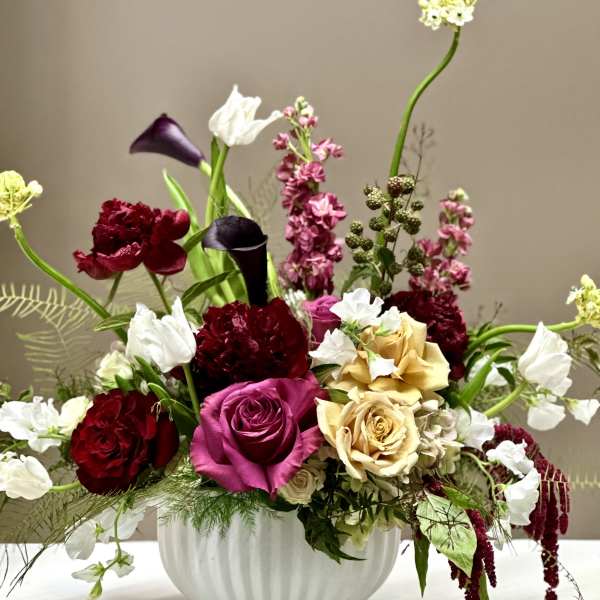 Mixed bouquet of roses, calla lilies, and white blooms in a white vase