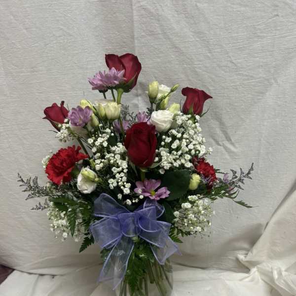 Mixed bouquet of red roses, white blooms, and purple flowers in a glass vase