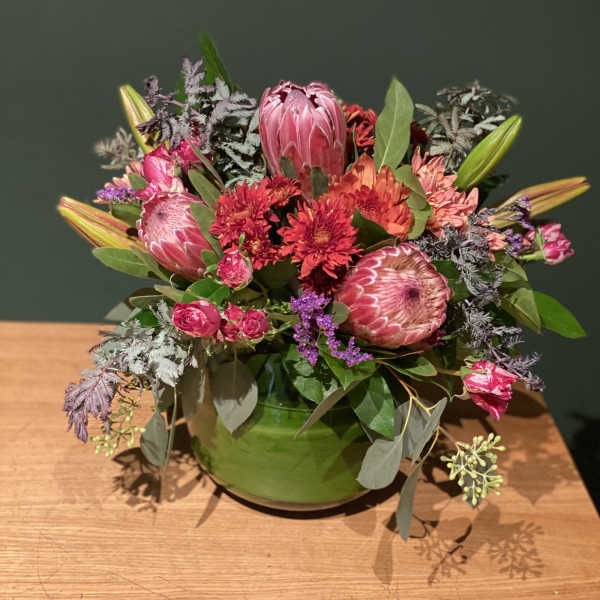 Pink and red mixed flower arrangement in a green bowl vase
