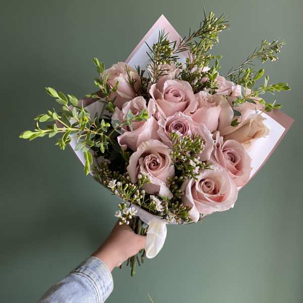 Handheld bouquet of pale pink roses with small white filler flowers
