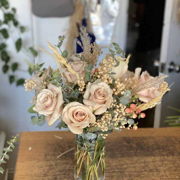 Blush roses arranged in a clear glass vase with dried grasses and filler flowers.