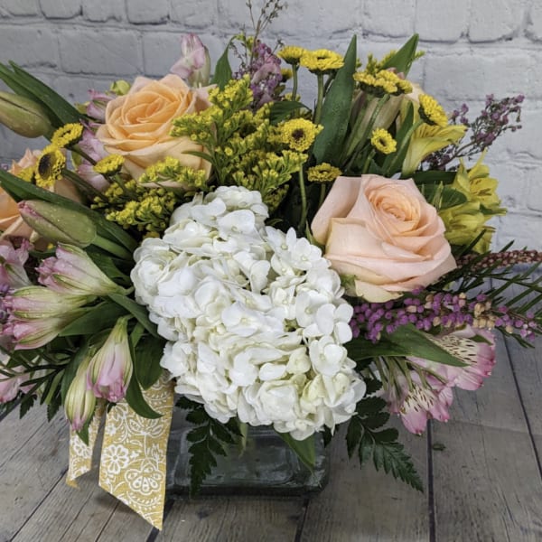 Mixed bouquet with peach roses, white hydrangea, and yellow accents in a glass vase