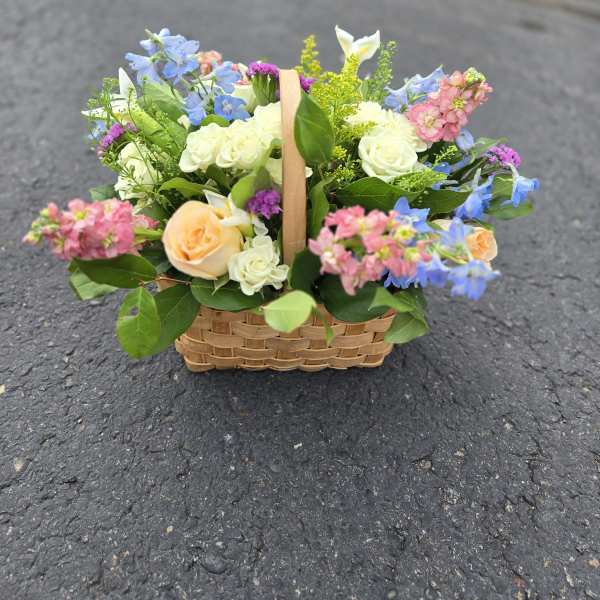 Basket of mixed pastel flowers with roses and blue blooms