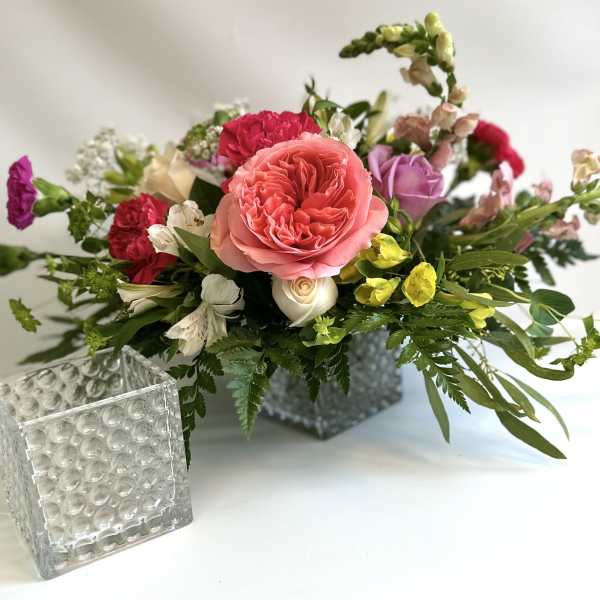 Mixed bouquet in a square glass vase with pink, red, purple, and yellow flowers