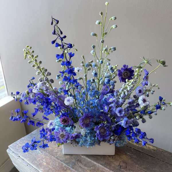 Blue and purple floral arrangement in a white rectangular vase