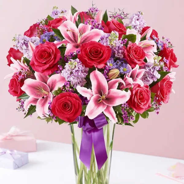 Bouquet of red roses and pink lilies in a clear glass vase with a purple ribbon