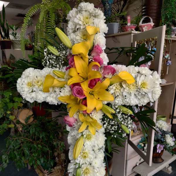 Cross-shaped floral tribute with white blooms, yellow lilies, and pink roses