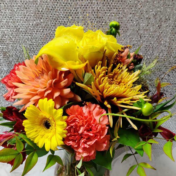 Bright mixed bouquet in a clear glass vase with yellow, peach, and coral blooms.