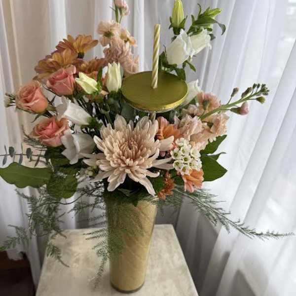 Tall floral arrangement in a gold vase with a candle on top