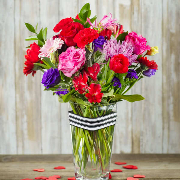 Mixed bouquet of red, pink, purple, and white flowers in a clear vase